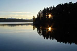 Landscape photograph of sun star shining through trees as viewed from Burnt Beach Campground on Vancouver Island. 