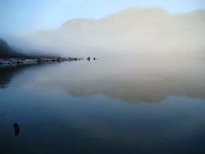 Landscape photography of mountains and their reflection showing through fog over Upper Campbell Lake on Vancouver Island.